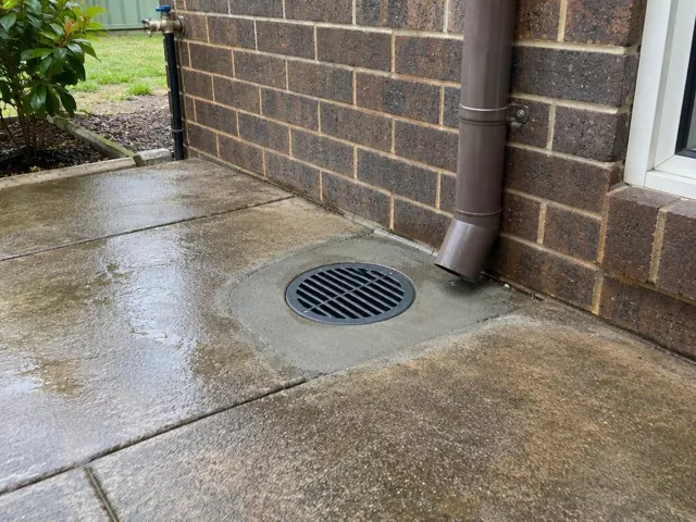 Outdoor drain grate beside brick wall and wet concrete paving in Fletcher