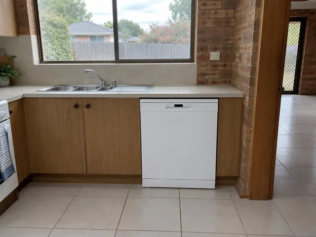 Kitchen bench with sink and white dishwasher beside wood cabinets and brick walls in Fletcher