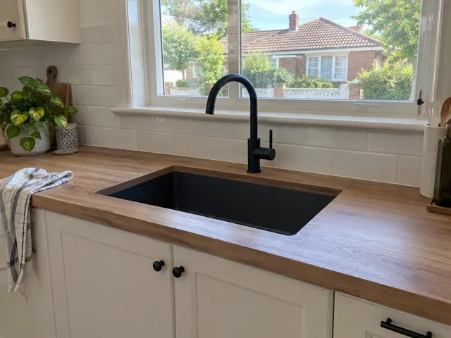 Black kitchen mixer tap over a black sink with timber benchtop and tiled splashback in Wallsend